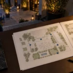 Plan du site et arrangements sur le plan d’aménagement posé sur le bureau avec une lampe et un stylo.